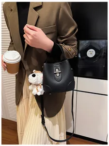 Detail of black pebbled leather bucket bag with silver lock and plush puppy charm