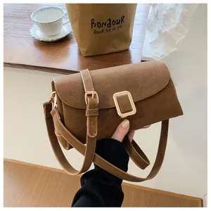 Detail of a brown suede crossbody bag featuring a square gold buckle in a French style