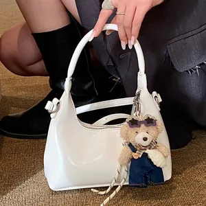 White glossy PU handbag with cute bear charm and metal zipper shown in street style