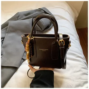 Detail einer Vintage-Lederhandtasche mit Goldprägung und dekorativem Perlenanhänger