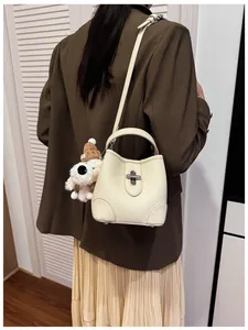 Detail of creamy white pebble leather bucket bag with silver lock and plush dog charm