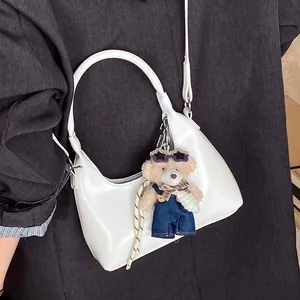 White semi-moon Hobo bag with teddy bear pendant worn on dark suit jacket