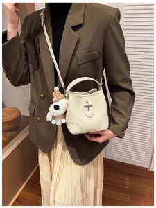 Detail of a beige bucket bag with metal clasp and a cute plush dog charm on a model