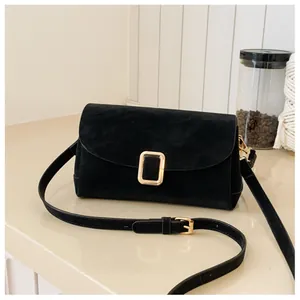 Detail of black suede shoulder bag featuring a gold rectangular buckle and smooth arc flap