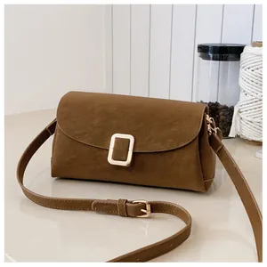 Macro view of a brown suede crossbody bag showing the golden metal buckle and texture