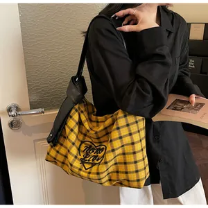 Close-up of yellow plaid tote bag featuring embroidered heart and black leather strap