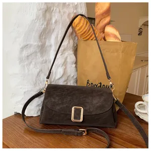 Detail of a dark brown suede crossbody bag with a large gold buckle on a wooden surface