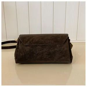 Detail shot of a dark brown suede square bag with fine stitching and golden hardware