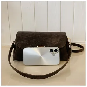Detail of dark brown suede square bag with gold buckle next to a phone for scale