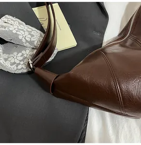 Detail of a brown oil wax leather shoulder bag with a silver zipper on a gray blazer background
