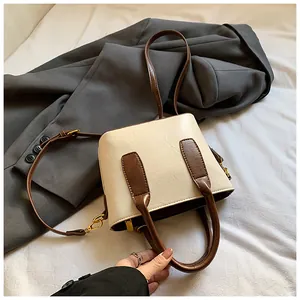 Detail einer cremeweißen Handtasche mit dunkelbraunen Riemen auf einem grauen Blazer