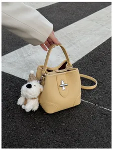 Detail of yellow lychee leather bucket bag with silver lock and white plush puppy charm