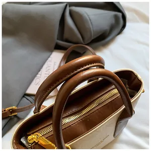 Detail der cremefarbenen Ledertasche mit glattem Goldreißverschluss und braunem Besatz