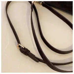 Detail view of adjustable dark brown suede shoulder strap with polished gold hardware