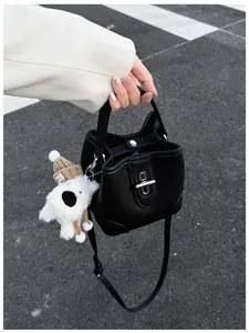 Detail of black leather bucket bag with silver clasp and white plush dog charm