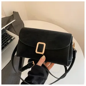 Detail of black suede shoulder bag featuring a rectangular gold buckle on a white table