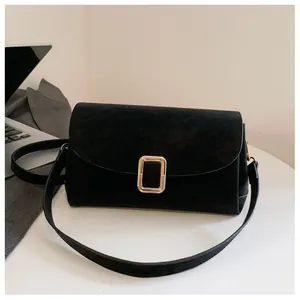 Detail of the black suede crossbody bag with elegant gold metal buckle on a white table