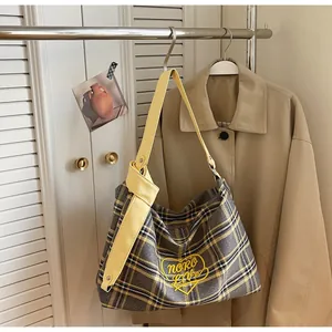 Detail of grey plaid tote bag featuring yellow heart embroidery and knotted leather strap