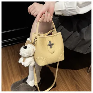 Detail of yellow pebbled leather bucket bag with silver turn-lock and plush puppy charm