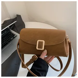 Detail view of a brown leather crossbody bag with a large square gold buckle on a desk