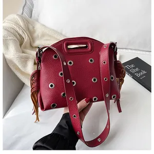 Dettaglio di borsa rosso scuro in pelle martellata con occhielli metallici e nappe