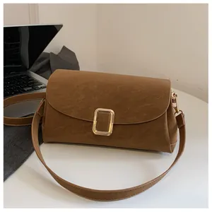 Close-up of brown suede crossbody bag with gold rectangular metal buckle on a desk