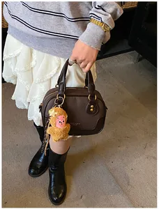 Detail of a dark brown matte leather handbag with vintage rivets and a plush monkey charm