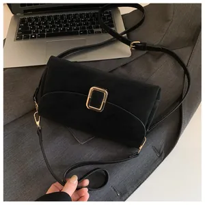 Detail of matte black leather square bag featuring a large gold metal buckle on a grey blazer