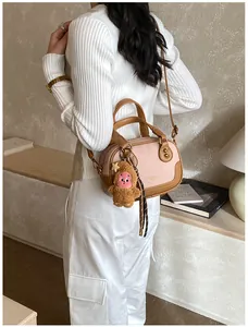Detail of pink bowling bag with brown leather trim, plush charm and crossbody strap