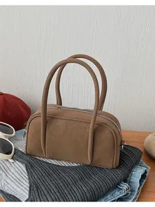 Borsa Boston cilindrica in pelle marrone su una scrivania con vestiti e accessori casual