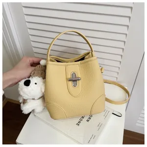Detail of yellow lychee leather bucket bag with silver turn-lock and plush puppy charm