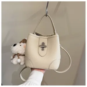 Close-up of beige lychee grain bucket bag with silver cross-lock and plush puppy pendant