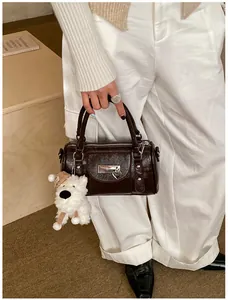 Detail einer braunen glänzenden Bowlingtasche aus Lackleder mit weißem Plüschwelpen-Anhänger