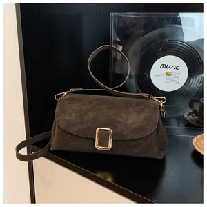 Detail of dark brown suede crossbody bag featuring a square gold metal buckle and leather strap