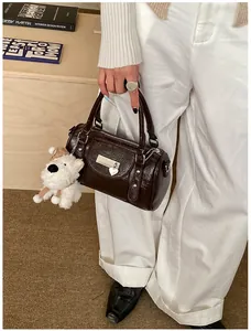 Detail der dunkelbraunen glänzenden Boston Bag mit Plüschhund-Anhänger und Herz-Anhänger