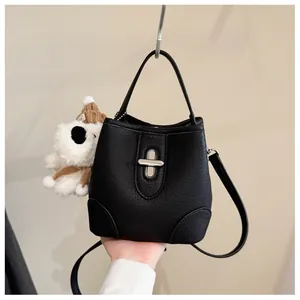 Detail of black pebbled leather bucket bag with silver clasp and plush bear charm