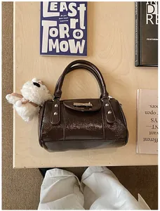 Detail der dunkelbraunen Lackleder-Bowlingtasche mit Silbernieten und Plüsch-Anhänger