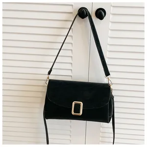 Macro shot of black suede shoulder bag with a gold rectangular metal buckle on a white door