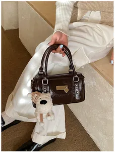 Detail einer dunkelbraunen Lackleder-Boston-Tasche mit süßem Bär-Anhänger und Nieten