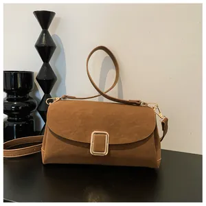 Close-up of brown suede square bag with gold metal buckle and detachable shoulder strap