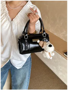 Detail der schwarzen glänzenden Polstertasche mit Metallteilen und Plüsch-Anhänger