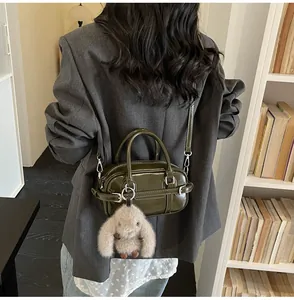 Detail of dark green patent leather handbag with a plush bunny charm on a model
