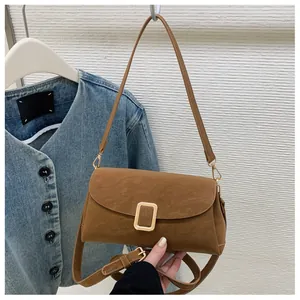 Close-up of brown suede shoulder bag with gold metal buckle and dual strap detail
