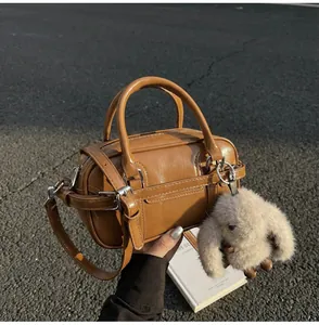 Close-up of caramel mini Boston bag with plush bunny charm on a textured outdoor background