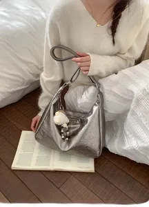 Close-up of metallic silver tote bag with soft pleated texture and plush ball charm