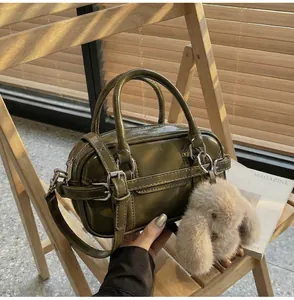 Macro detail of olive green bowling bag featuring a plush rabbit charm and silver zipper