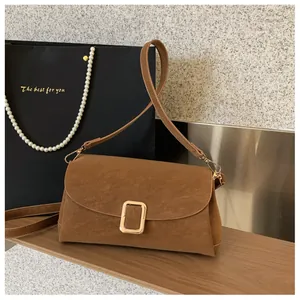 Detail of a brown suede shoulder bag with a gold rectangular buckle on a wooden shelf