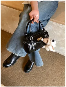 Detail der schwarzen Lackleder-Bowlingtasche mit Plüschwelpen-Anhänger und Metallplatte