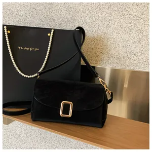 Detail of black suede square crossbody bag with gold buckle on an elegant display stand