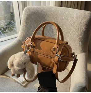 Detail of retro brown Boston bag with leather strap and plush bunny charm on sofa